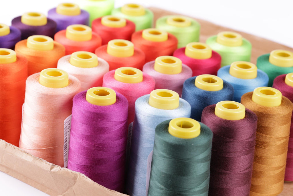 A cardboard box filled with various colored spools of thread, including pink, orange, green, blue, and purple.