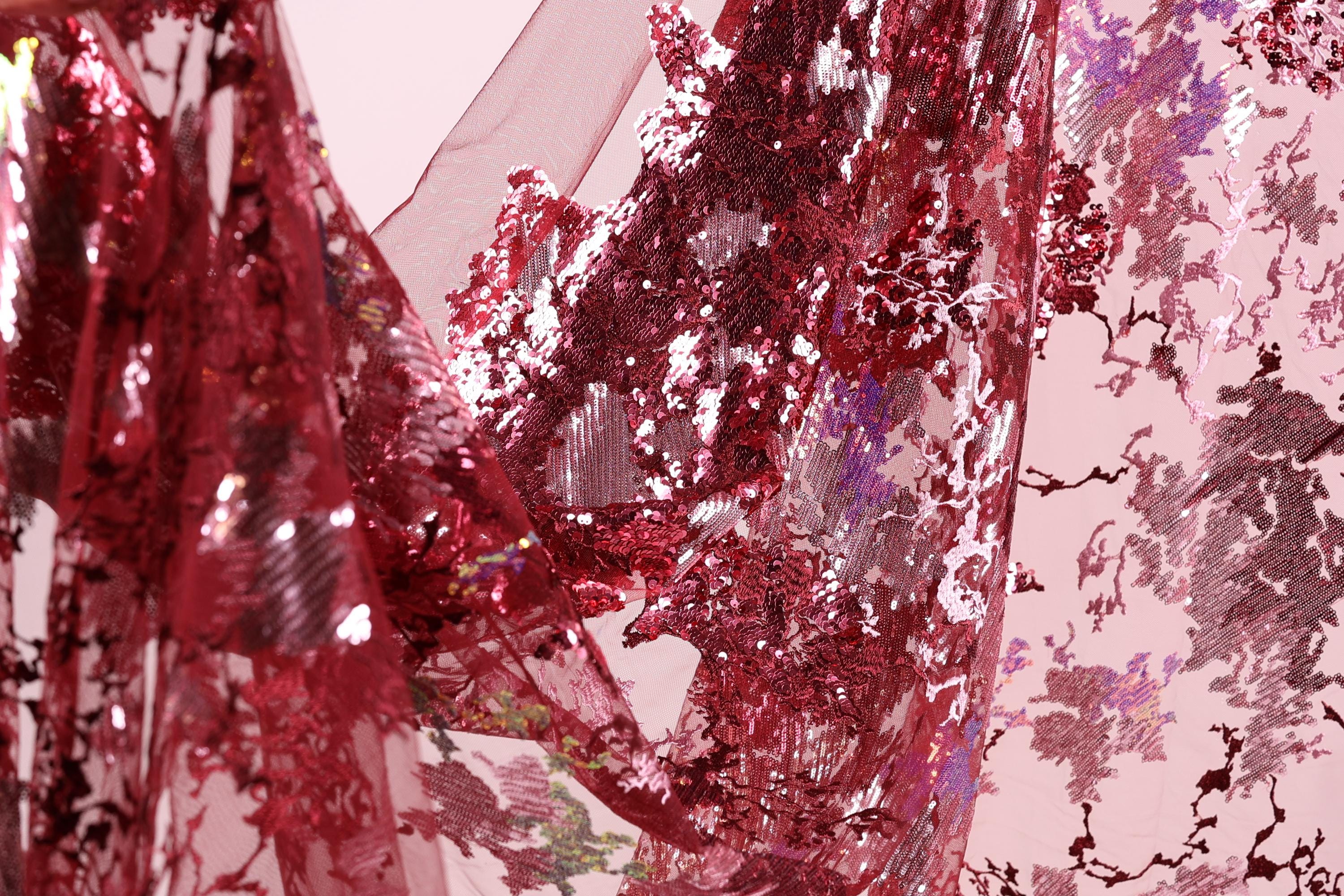 a close-up view of a fabric with a red and purple floral pattern, with a shiny, sequined texture.