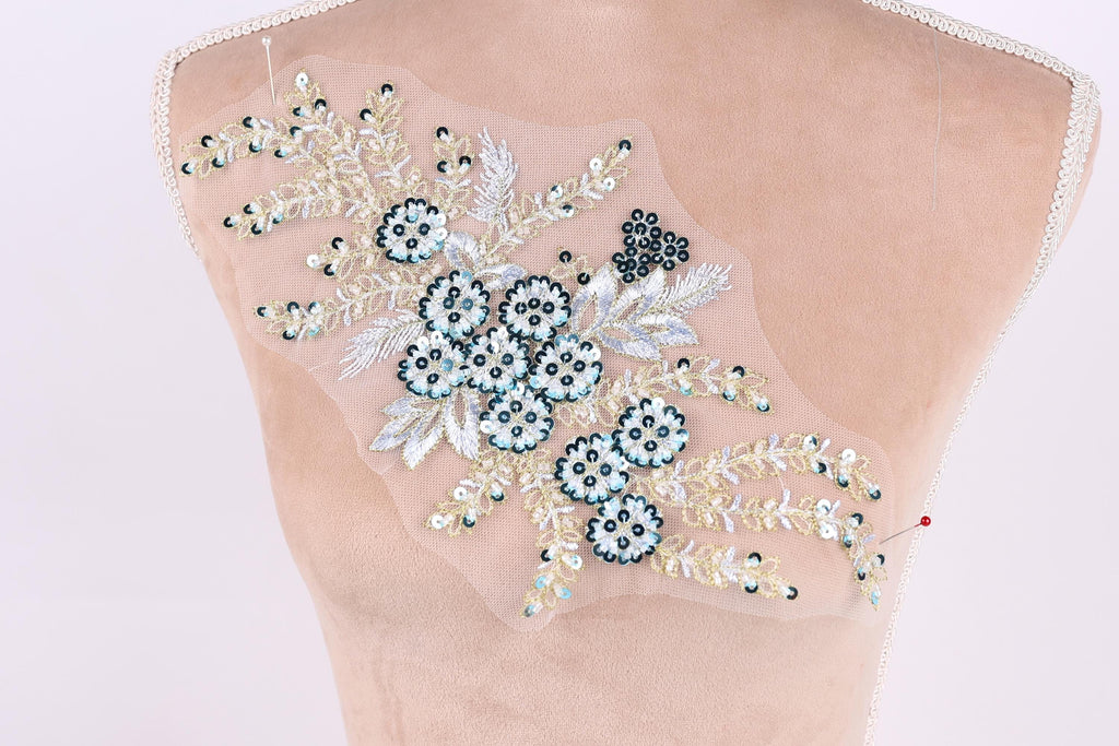a mannequin torso with a decorative floral embroidery on it. The embroidery features a variety of flowers and leaves in shades of blue and white, creating a visually appealing and intricate design.