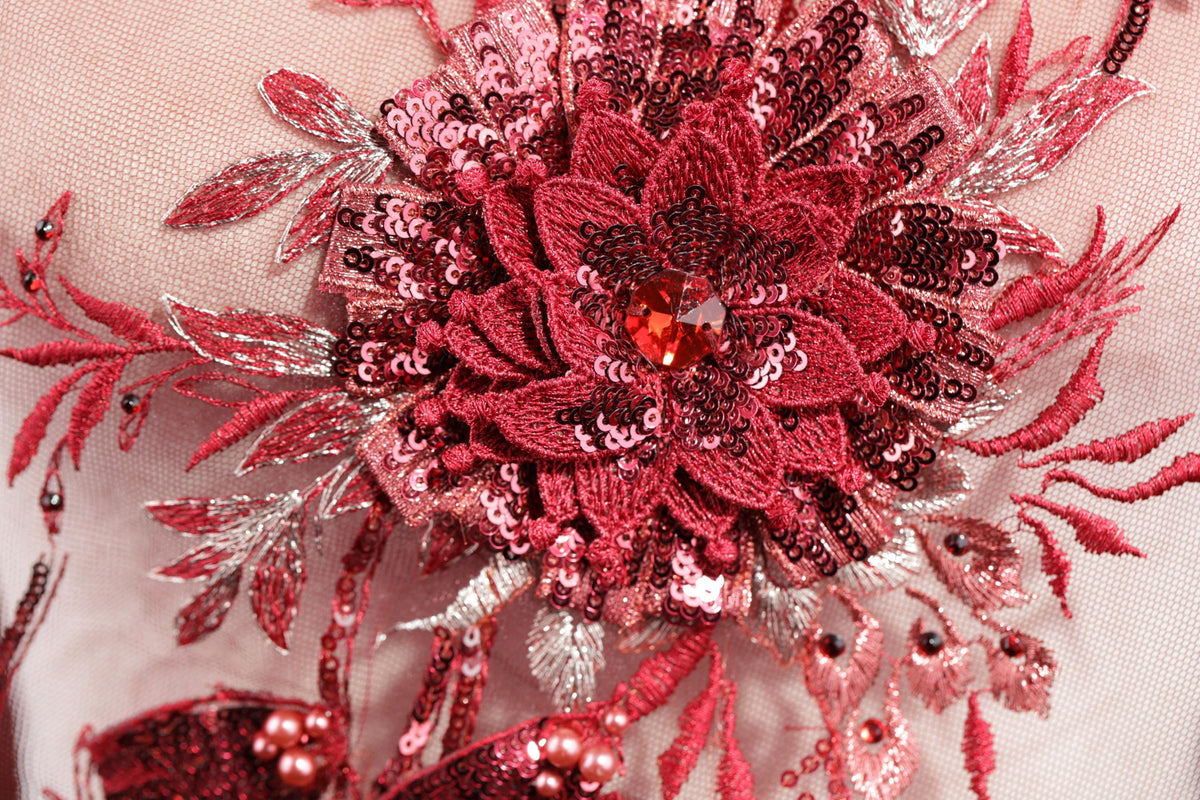 a close-up view of a red and pink floral embroidered piece, with intricate details and embellishments such as sequins and beads.