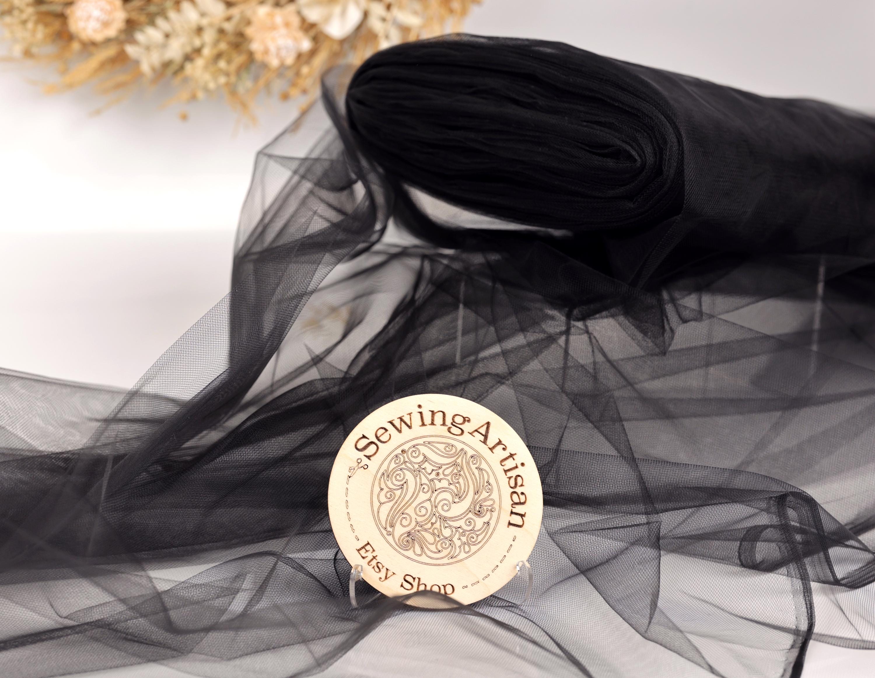 a black fabric, possibly silk or chiffon, with a round wooden plaque in the foreground displaying the text "SewingArtisan Etymological Shop".