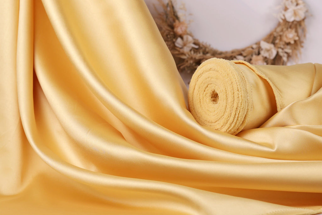 a close-up view of a yellow fabric, possibly silk or satin, with a wreath of flowers in the background.
