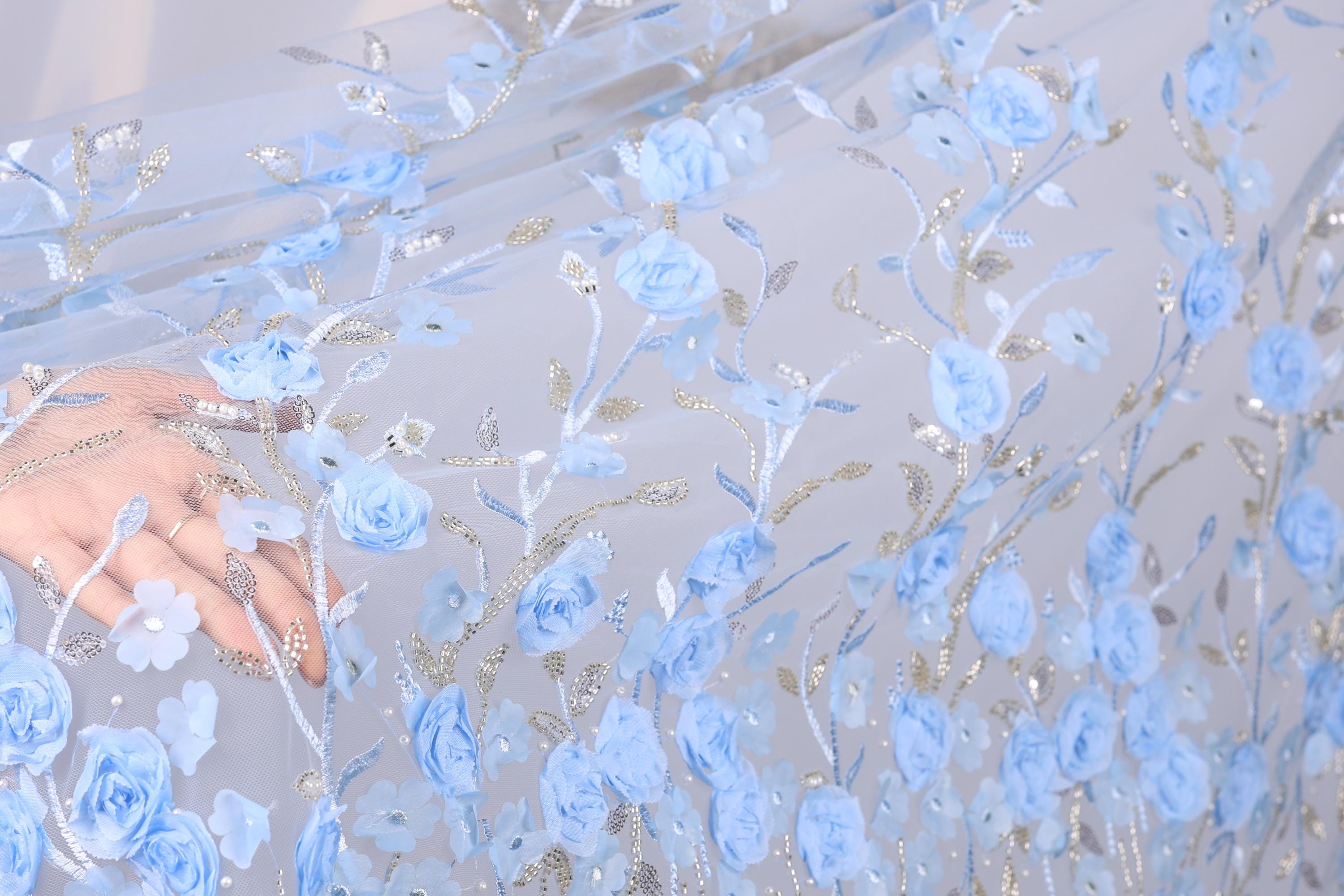 A close-up view of a hand holding a piece of fabric with a floral pattern of blue flowers and leaves.