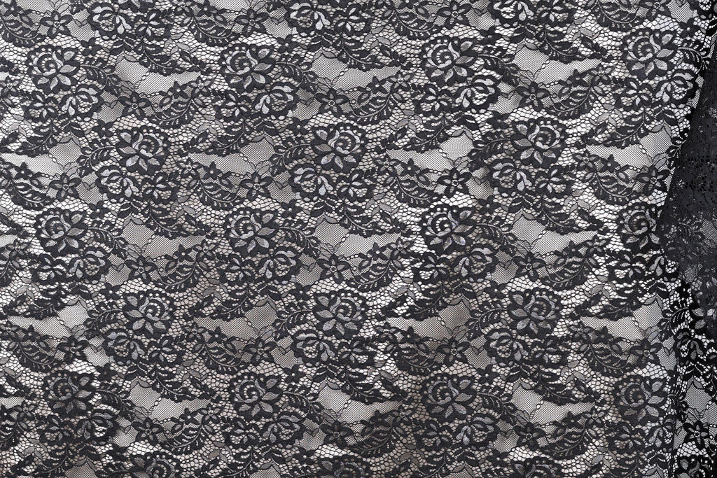 The image is a close-up of a black and white lace pattern, featuring intricate floral and leaf designs.