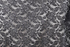 The image is a close-up of a black and white lace pattern, featuring intricate floral and leaf designs.