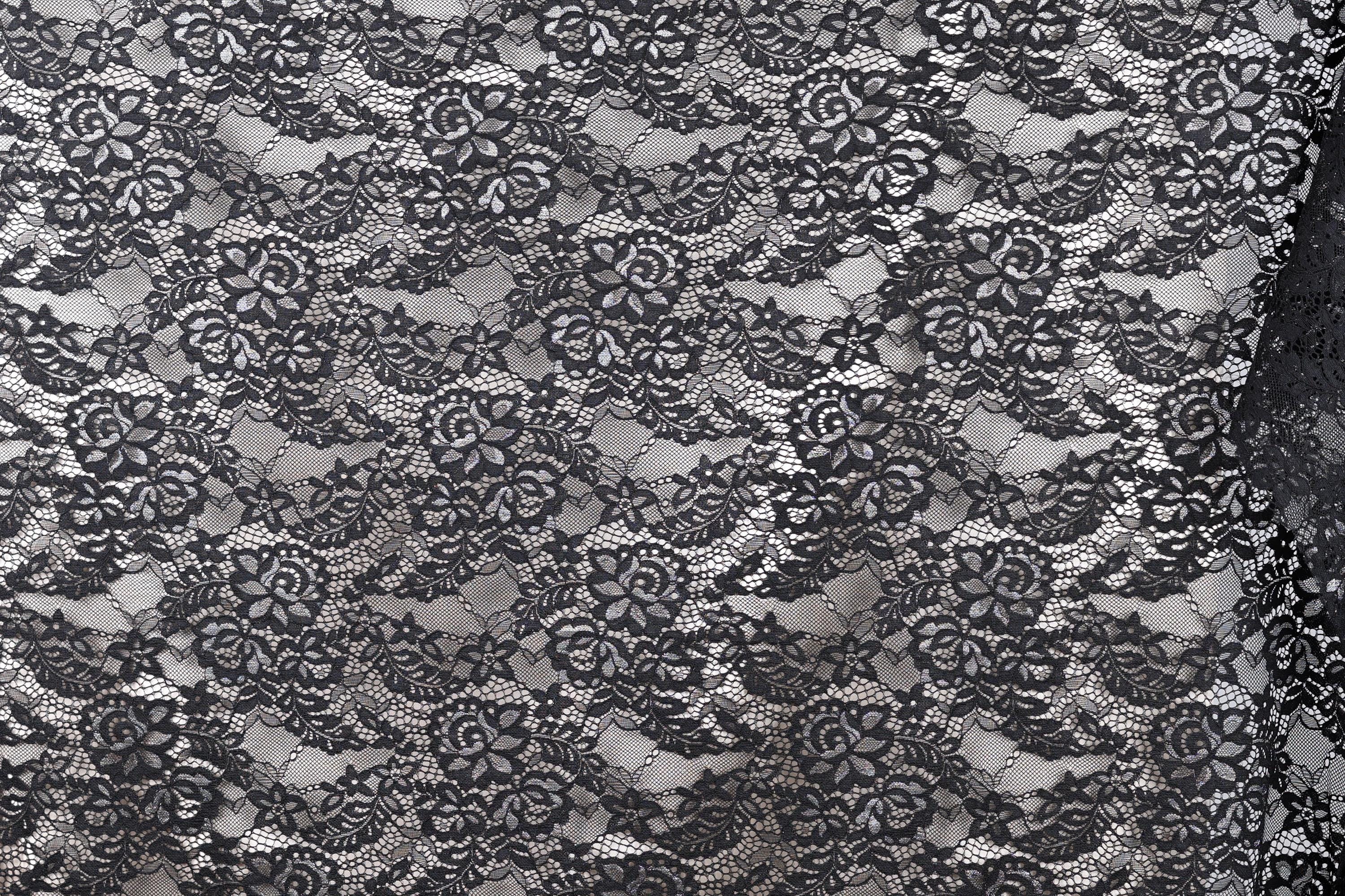 The image is a close-up of a black and white lace pattern, featuring intricate floral and leaf designs.