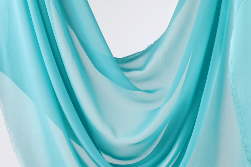 A close-up view of a light blue fabric, possibly a sheer or chiffon, with a soft, flowing texture.