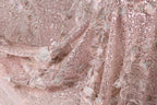 The image is a close-up of a fabric with a pink and white floral pattern, featuring sequins and lace-like elements.