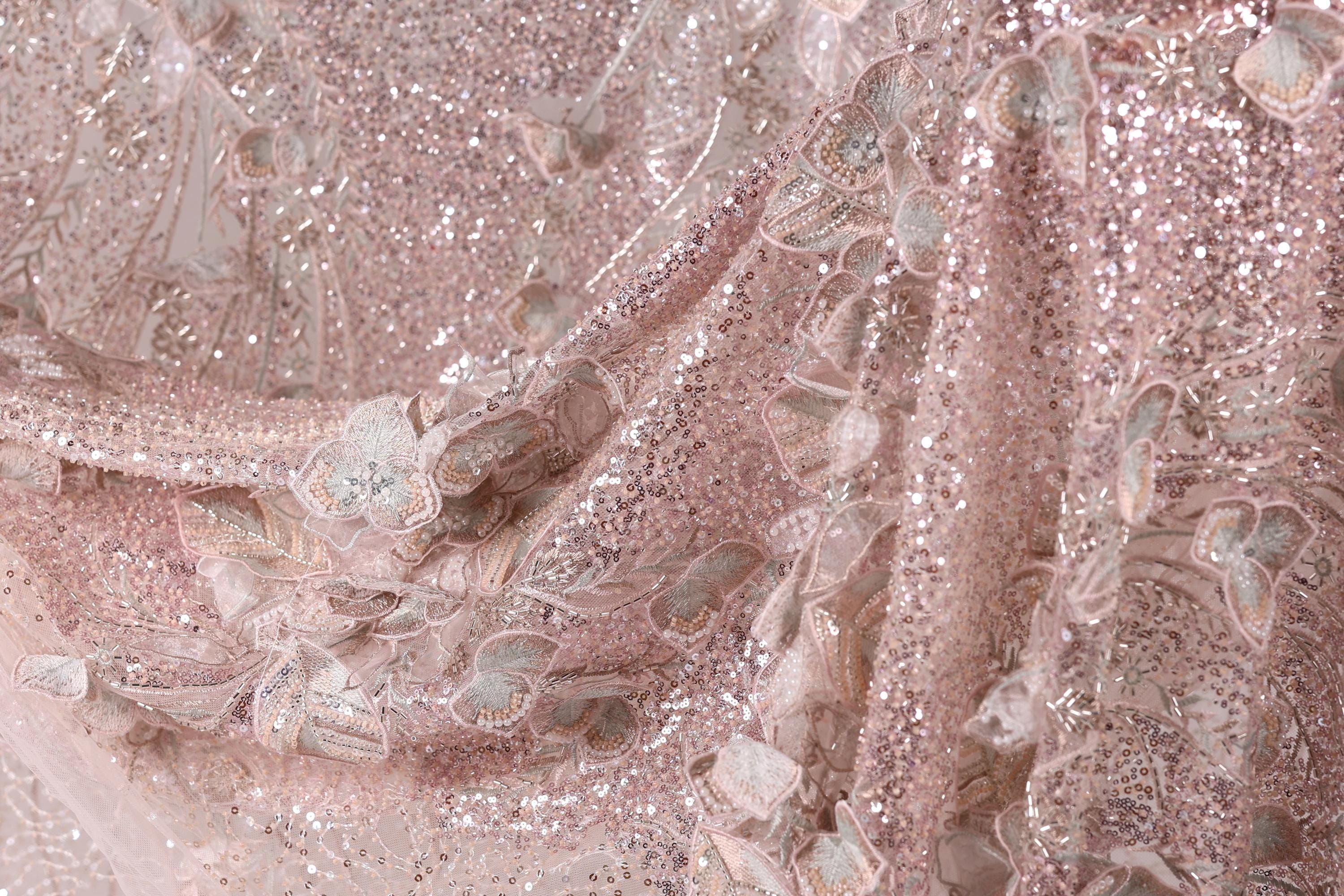 The image is a close-up of a fabric with a pink and white floral pattern, featuring sequins and lace-like elements.
