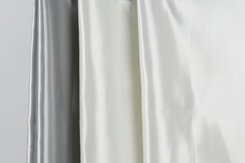 three different colored silks hanging side by side, with the middle one being white and the two on either side being silver.