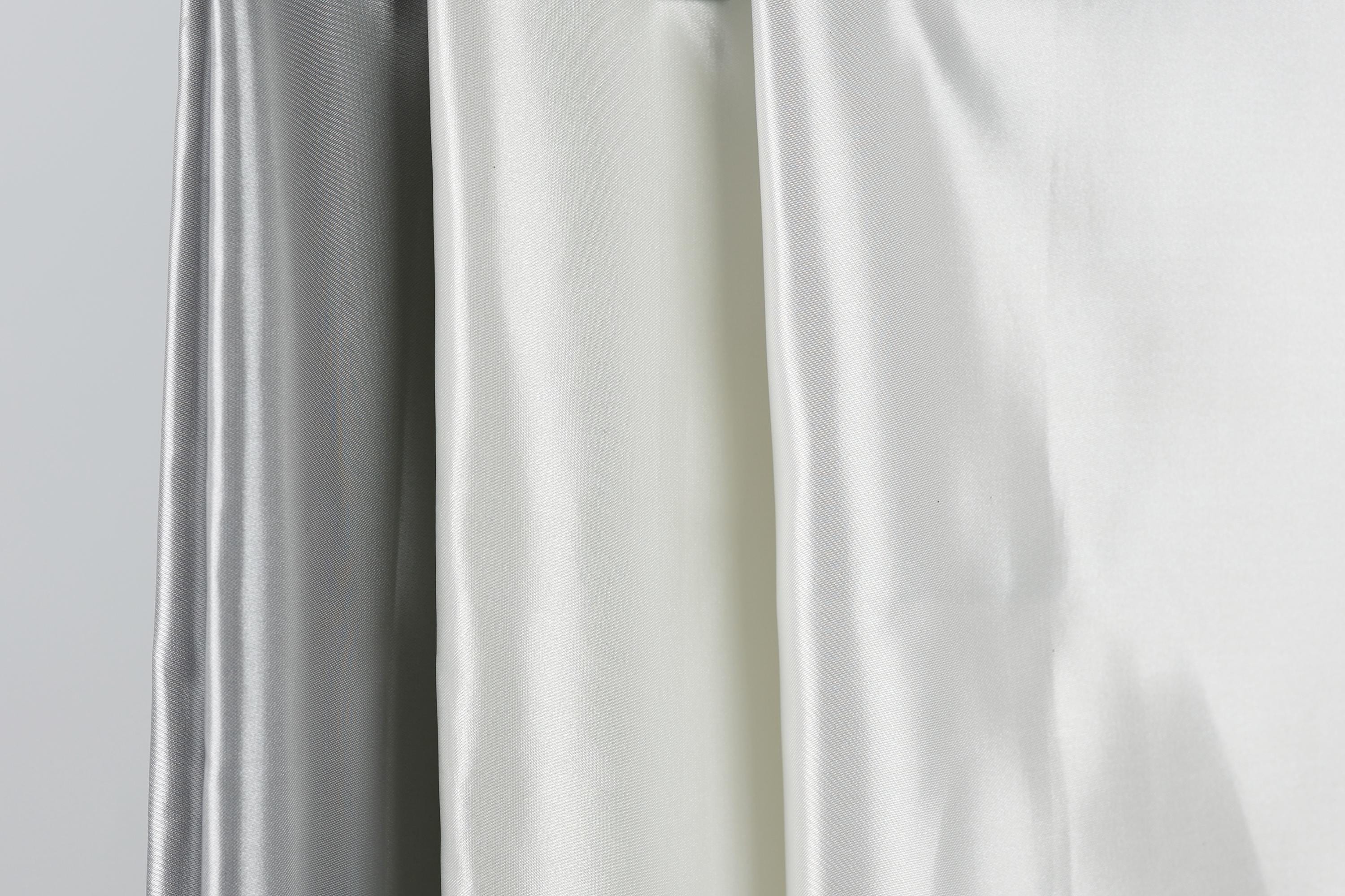 three different colored silks hanging side by side, with the middle one being white and the two on either side being silver.