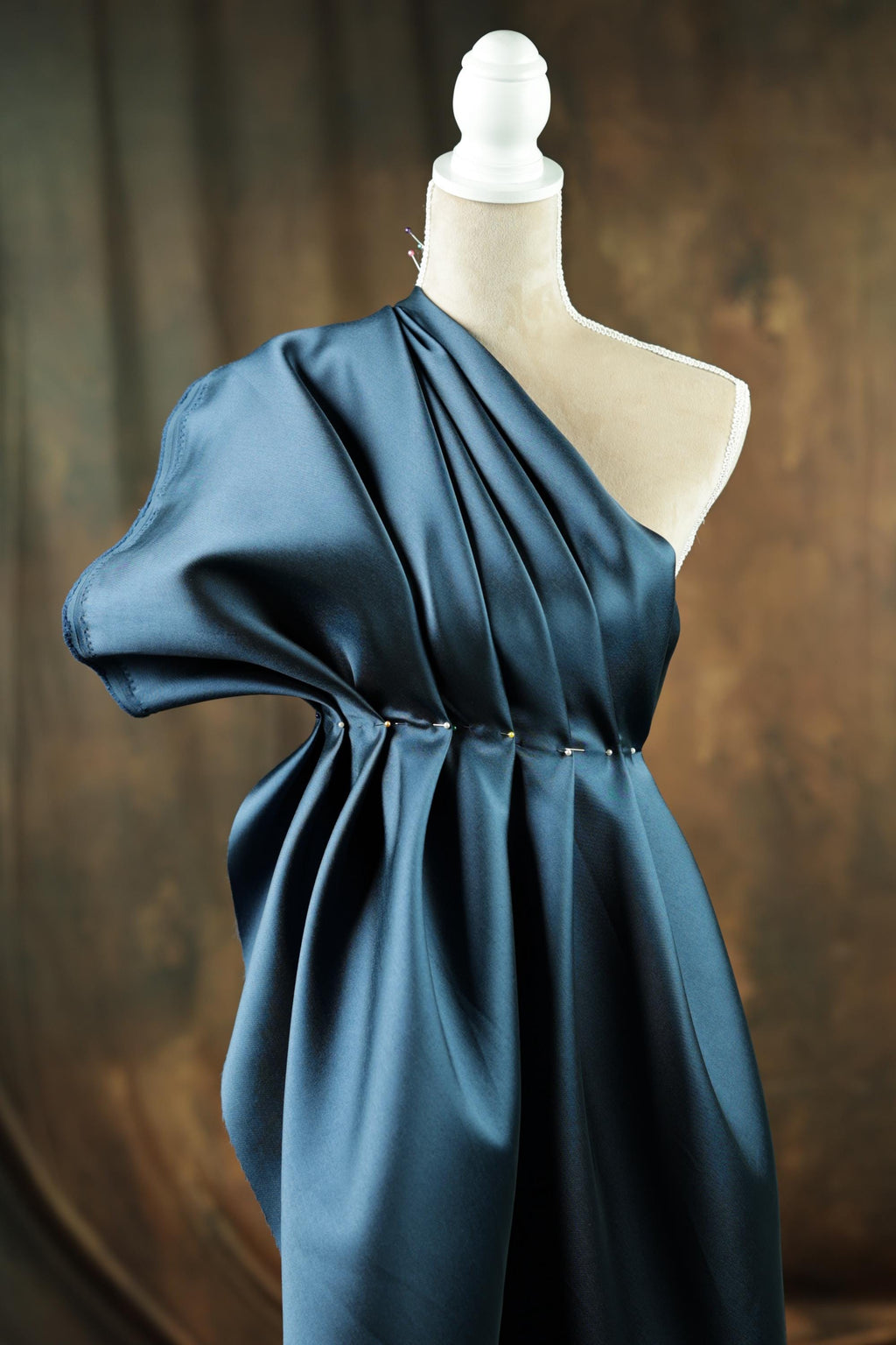 A close-up view of a blue satin fabric draped over a mannequin head, with a white base and a white pole.