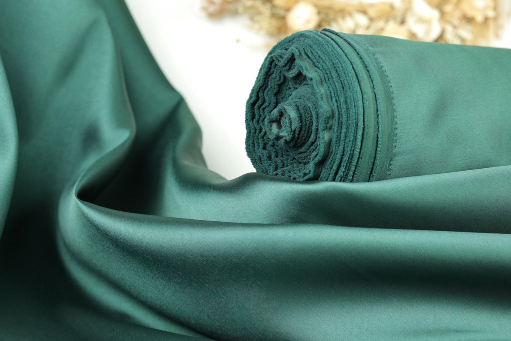 A close-up view of a green satin fabric, possibly silk, with a rolled-up end visible.