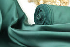 A close-up view of a green satin fabric, possibly silk, with a rolled-up end visible.