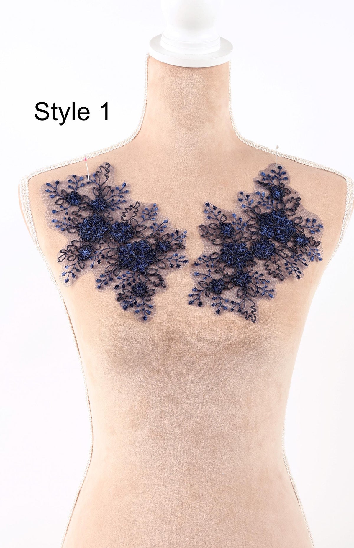 A mannequin wearing a beige dress with blue floral lace appliques on the chest area.