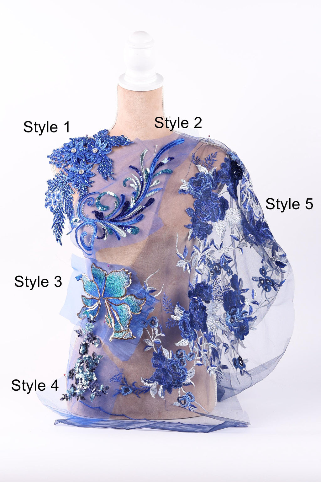 A mannequin wearing a dress with intricate blue floral embroidery and a sheer, flowy fabric overlay.