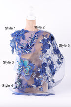 A mannequin wearing a dress with intricate blue floral embroidery and a sheer, flowy fabric overlay.
