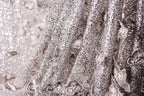 The image is a close-up of a fabric with a silver sequin pattern, featuring a delicate floral design.