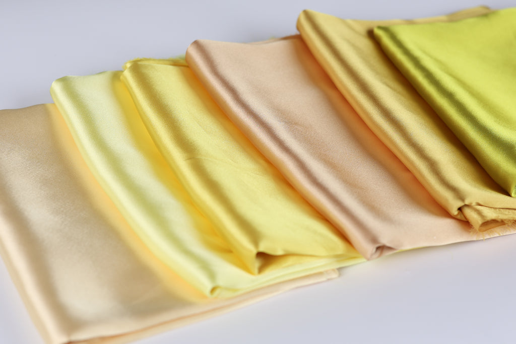 A row of folded fabric pieces in various shades of yellow, ranging from pale to deep, arranged on a white surface.