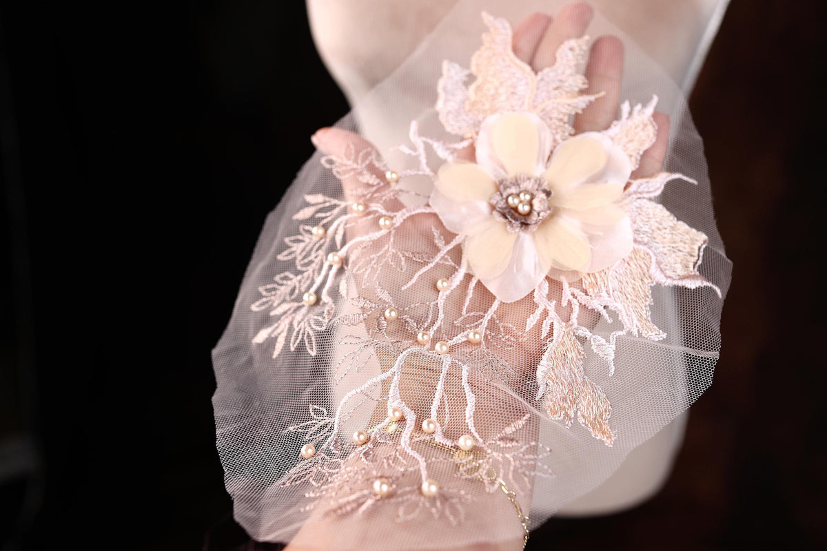 A hand holding a delicate, intricately designed flower made of lace and pearls against a dark background.