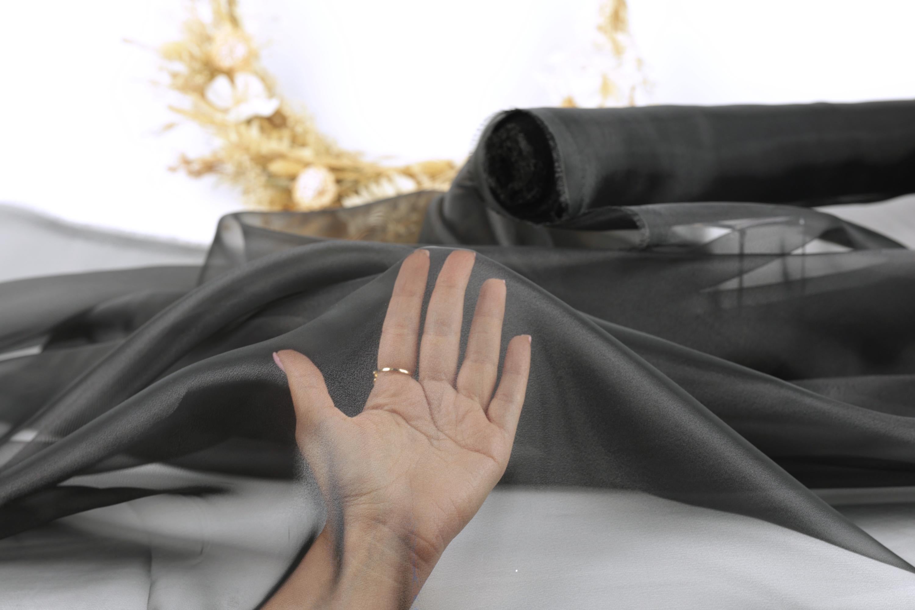 A hand is holding up a piece of black fabric, which appears to be a sheer material, against a blurred background.