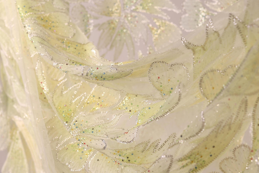 The image is a close-up of a fabric with a floral pattern, featuring yellow and green colors and small, multicolored beads or sequins.