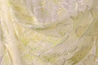 The image is a close-up of a fabric with a floral pattern, featuring yellow and green colors and small, multicolored beads or sequins.