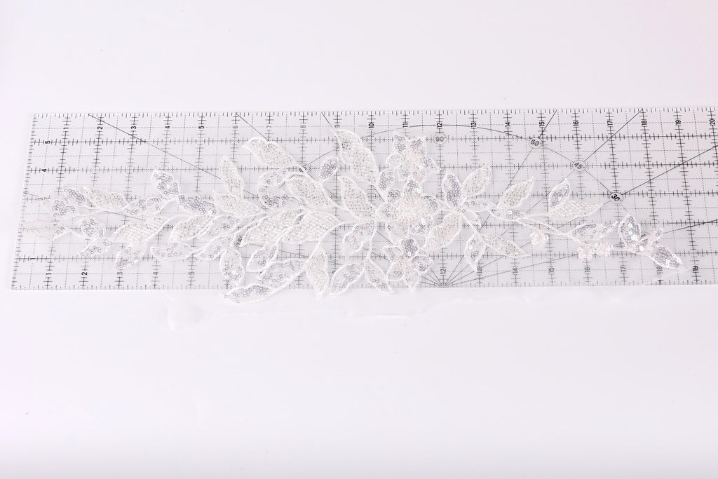 a piece of white lace with a floral pattern, placed on a transparent ruler.