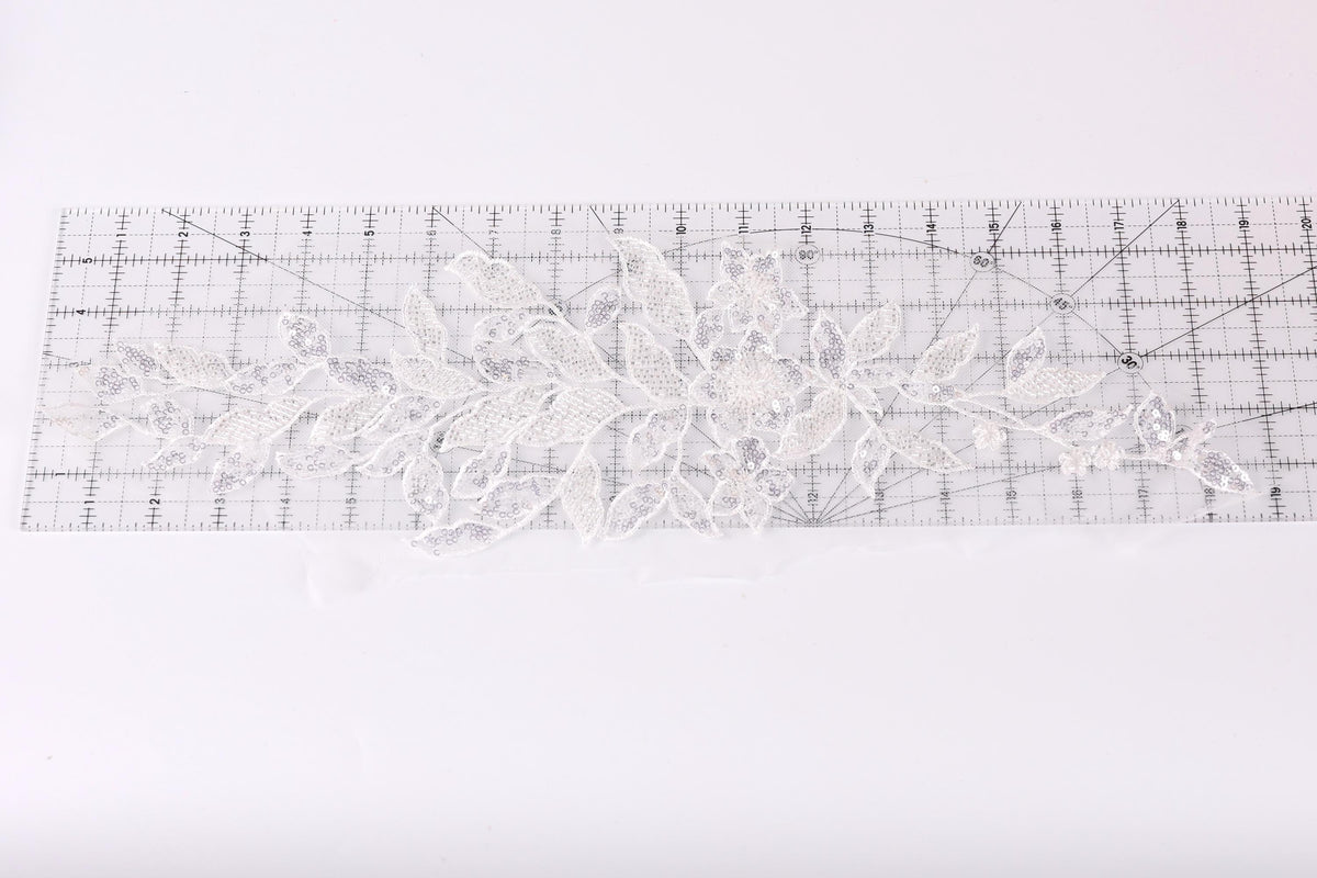 a piece of white lace with a floral pattern, placed on a transparent ruler.