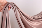 A hand holding a piece of light brown fabric, possibly silk or chiffon, with the fabric being curled and draped.
