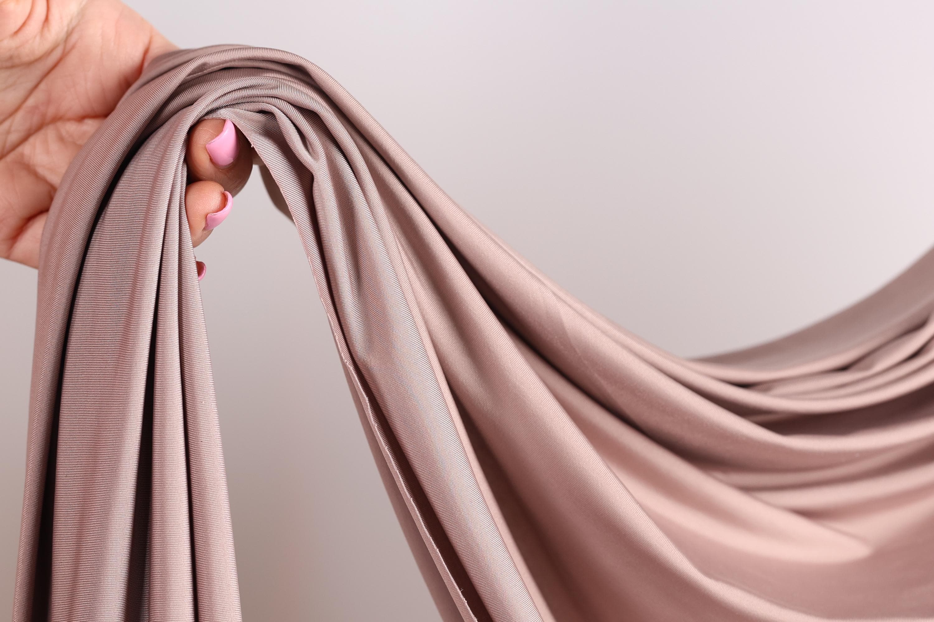 A hand holding a piece of light brown fabric, possibly silk or chiffon, with the fabric being curled and draped.