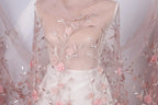 A mannequin wearing a white dress with pink floral embroidery and a sheer pink fabric draped over it.