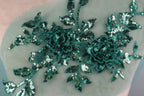 a close-up view of a delicate, intricate floral embroidery with a green and white color scheme. The embroidery is composed of numerous small sequin flowers and leaves, creating a visually striking and detailed design.