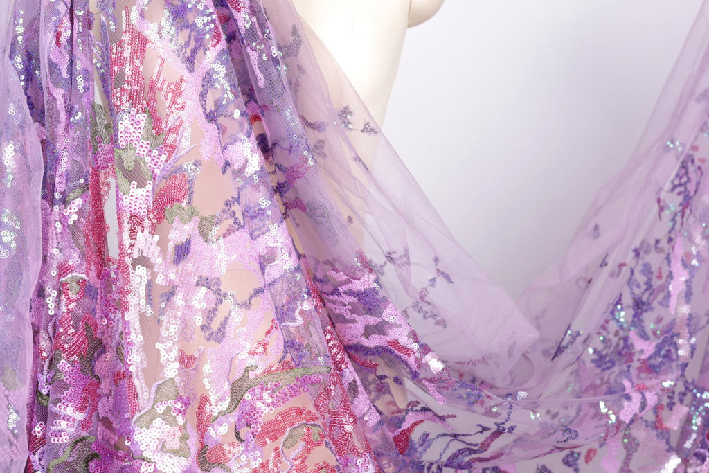 a close-up view of a fabric with a floral pattern, predominantly in shades of purple and pink. The fabric appears to be made of sheer material, giving it a delicate and airy appearance. The image does not contain any text or other discernible objects or actions.