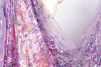 a close-up view of a fabric with a floral pattern, predominantly in shades of purple and pink. The fabric appears to be made of sheer material, giving it a delicate and airy appearance. The image does not contain any text or other discernible objects or actions.