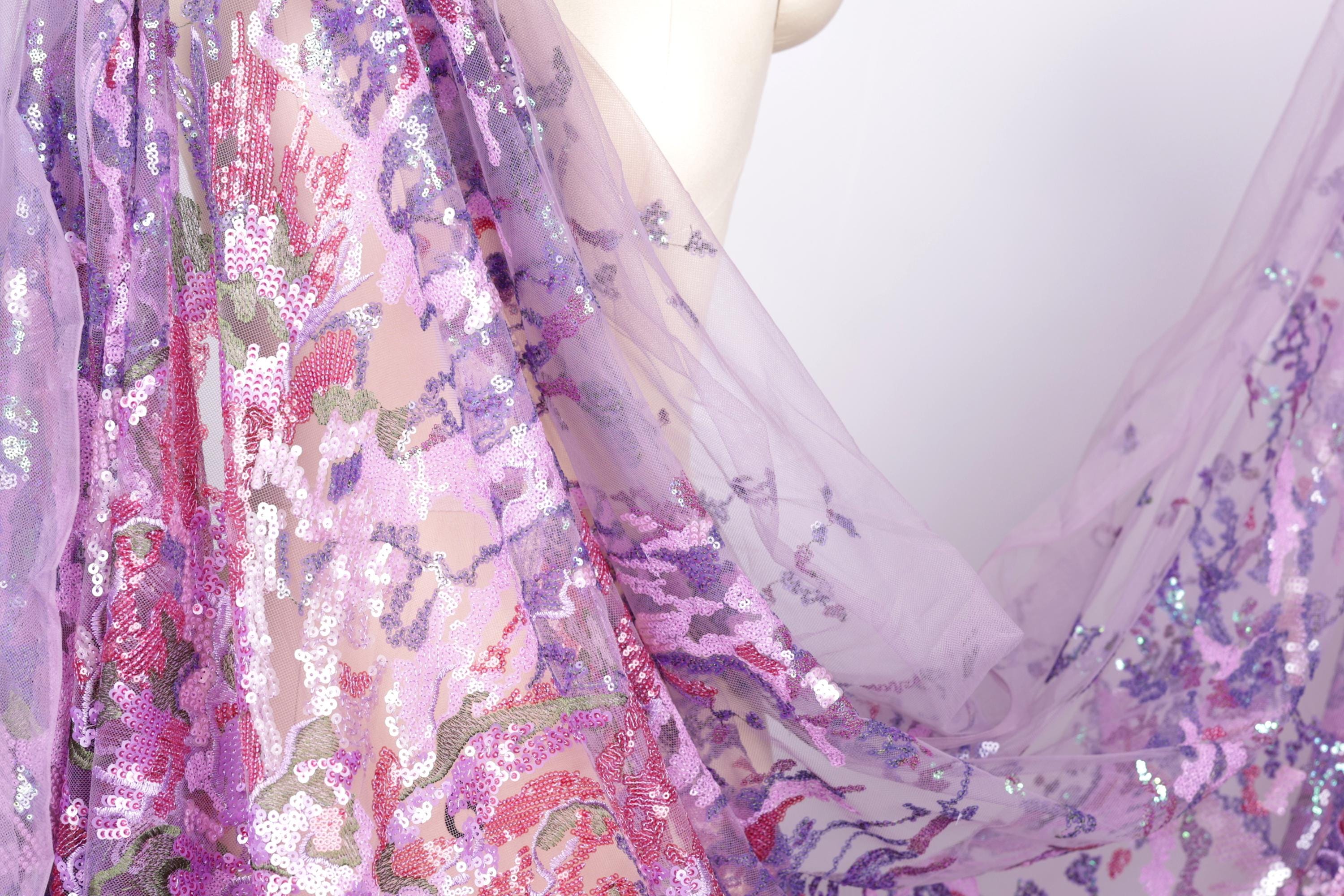 a close-up view of a fabric with a floral pattern, predominantly in shades of purple and pink. The fabric appears to be made of sheer material, giving it a delicate and airy appearance. The image does not contain any text or other discernible objects or actions.