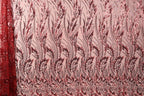 a close-up view of a fabric with a repeating pattern of red and black floral designs. The pattern is intricate and detailed, with the flowers and leaves appearing in various sizes and orientations. The fabric appears to be made of a material with a metallic or sequined texture, adding a touch of sparkle and shine to the overall design.