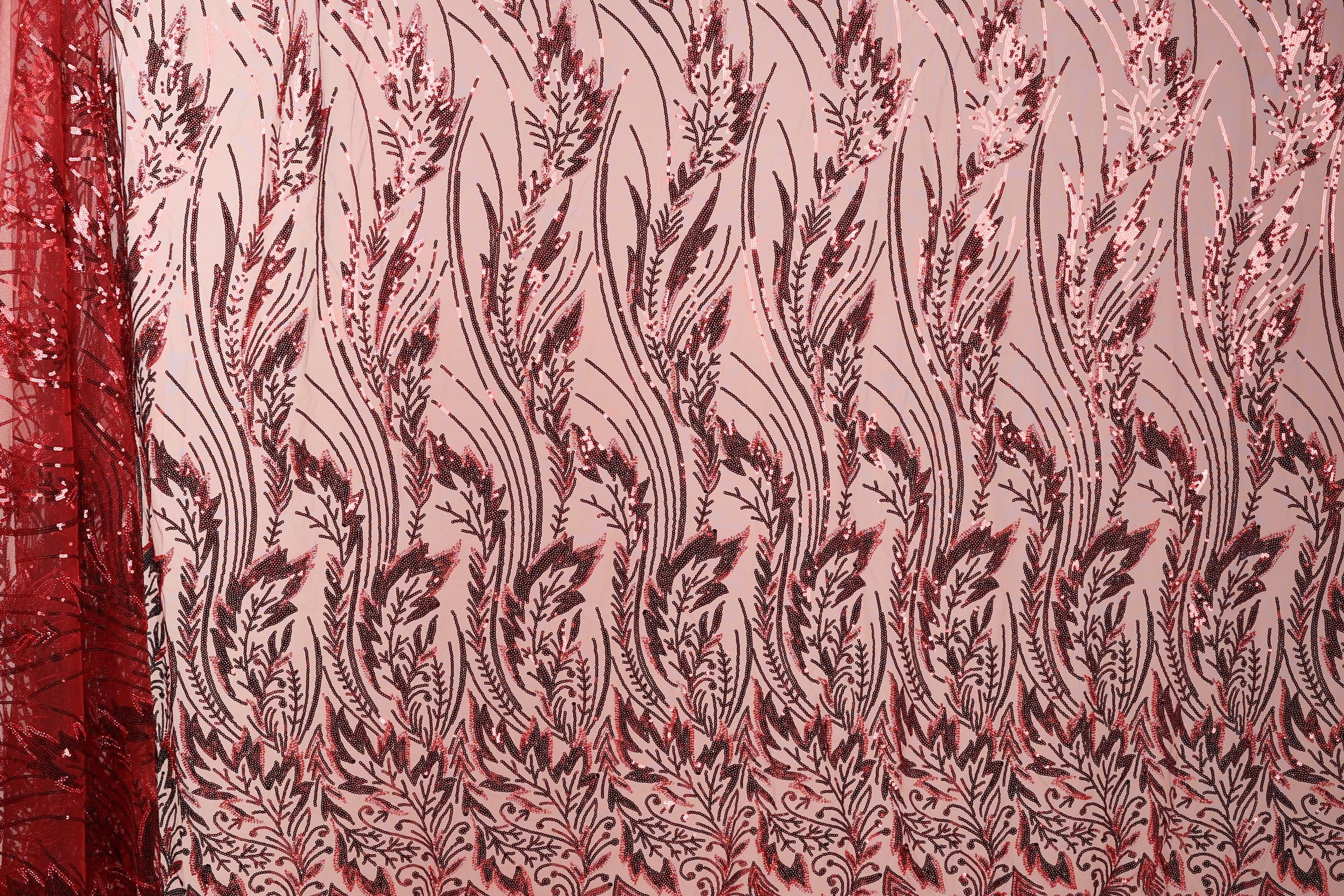 a close-up view of a fabric with a repeating pattern of red and black floral designs. The pattern is intricate and detailed, with the flowers and leaves appearing in various sizes and orientations. The fabric appears to be made of a material with a metallic or sequined texture, adding a touch of sparkle and shine to the overall design.