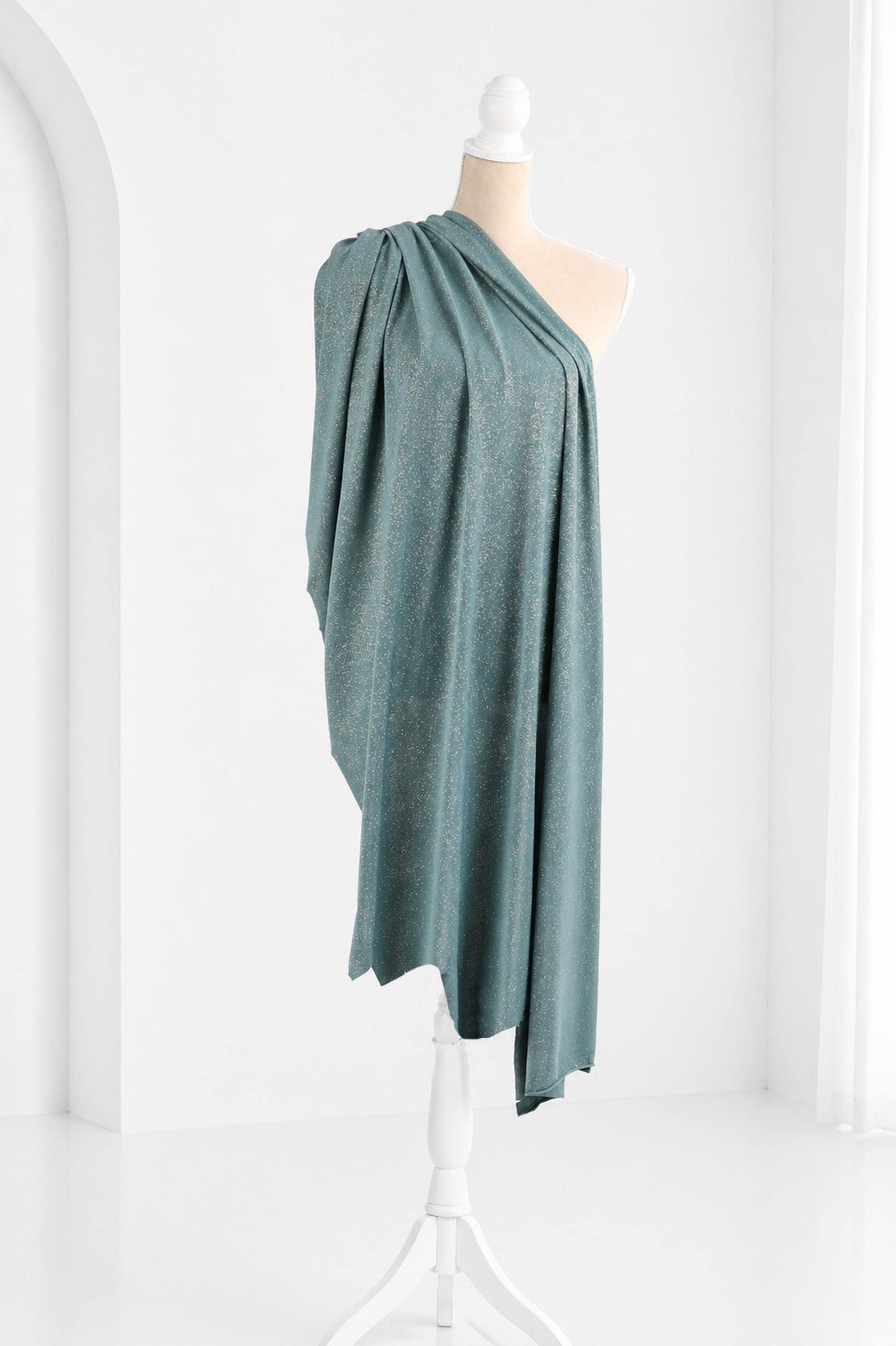 A mannequin wearing a teal-colored draped dress with a one-shoulder design, displayed on a white mannequin stand against a white background.