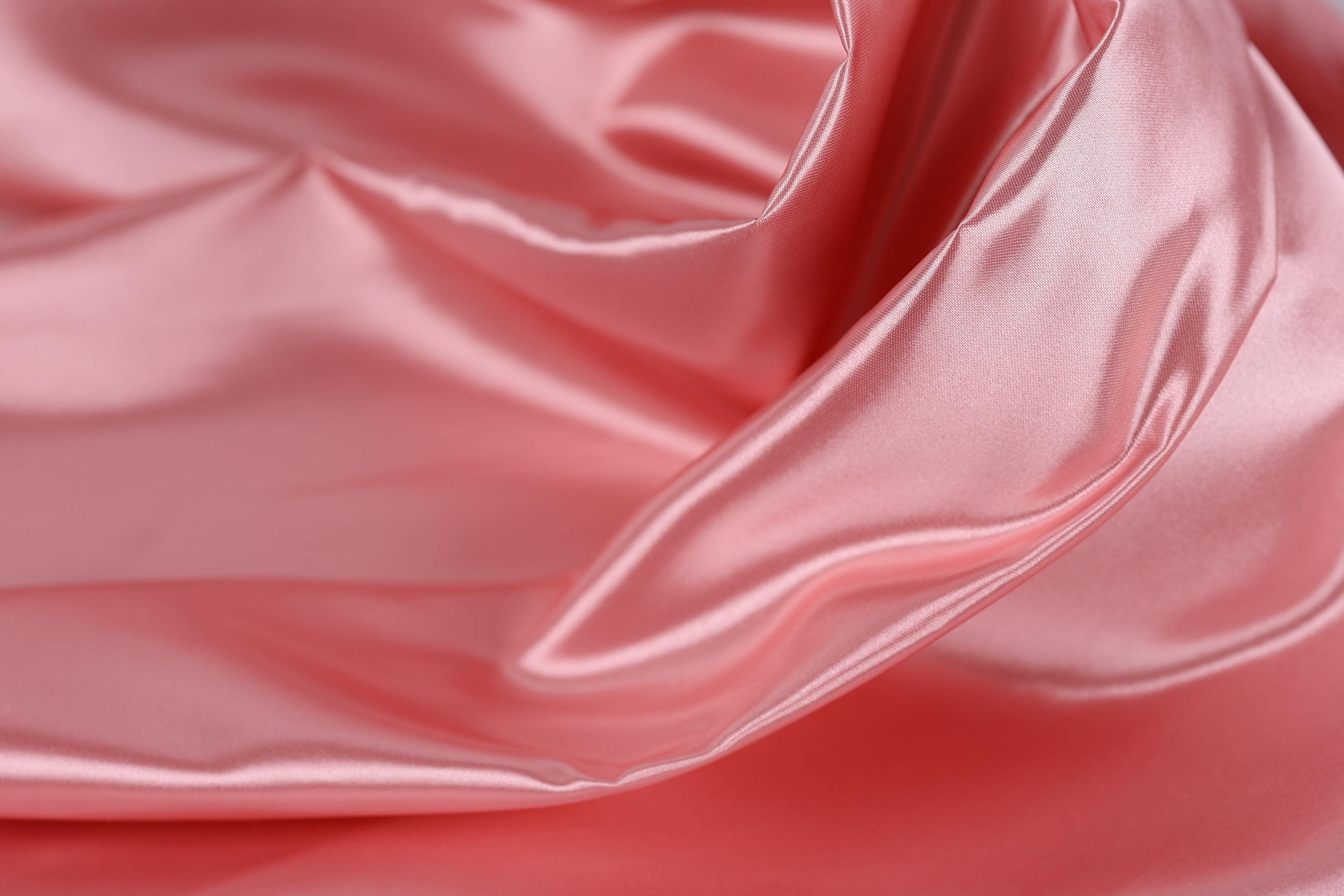 A close-up view of a soft, flowing pink satin fabric, with its smooth and shiny texture visible.