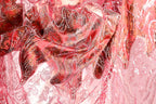 The image is a close-up of a fabric with a pink and red color scheme, featuring intricate patterns and designs. The fabric appears to be made of lace or a similar material, with a floral or leaf-like pattern. The image does not contain any text or other discernible objects or actions.