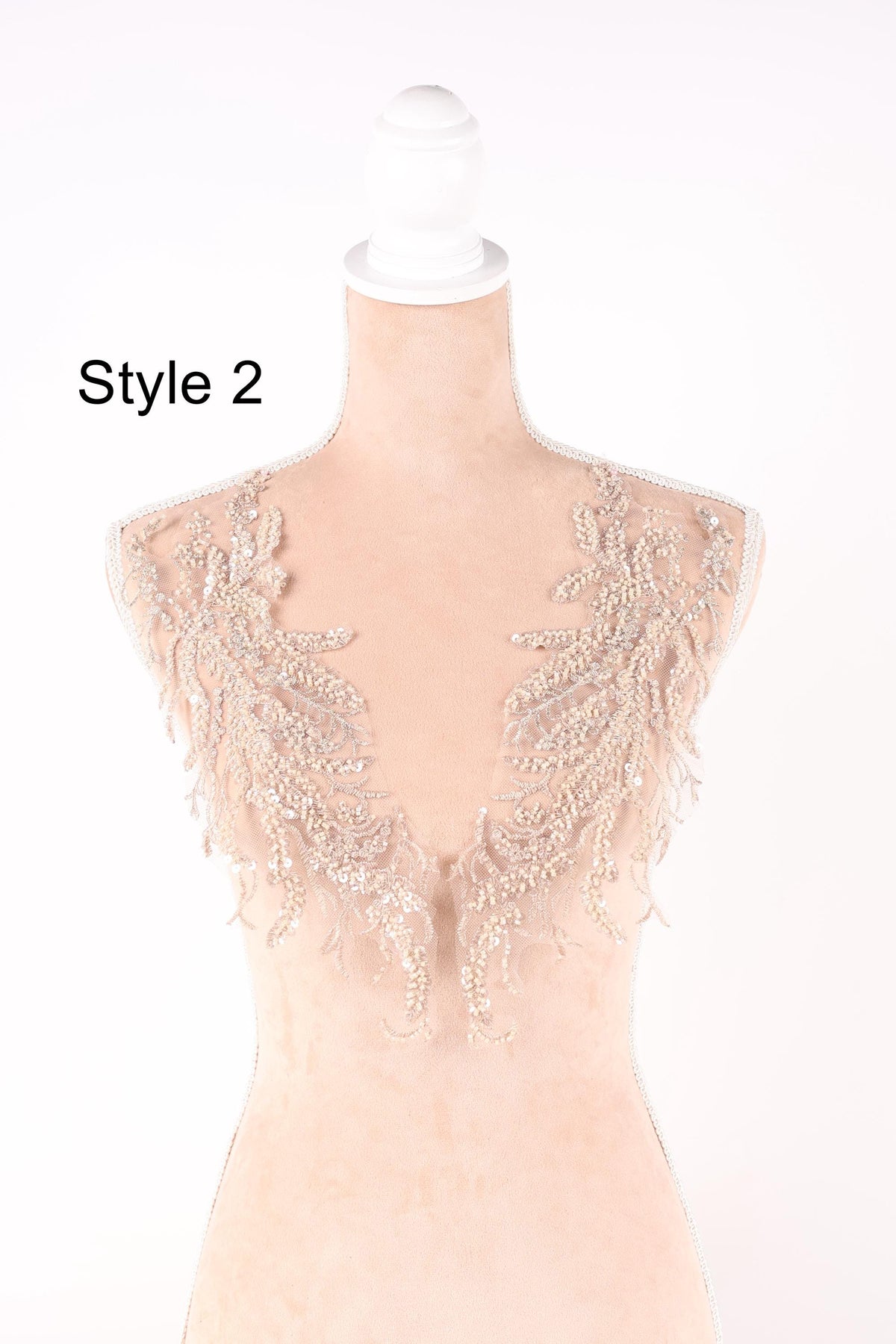 A mannequin wearing a beige dress with intricate lace and beaded embellishments on the neckline and shoulders.