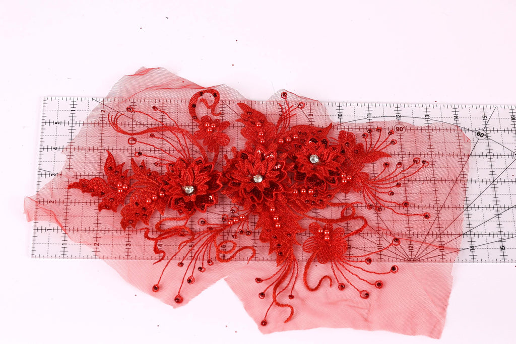 a red floral design with intricate details, including red flowers and red beads, placed on a transparent surface.