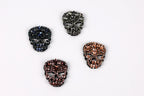 four ornate skull-shaped brooches, each with a unique color and design, arranged in a square formation against a white background.