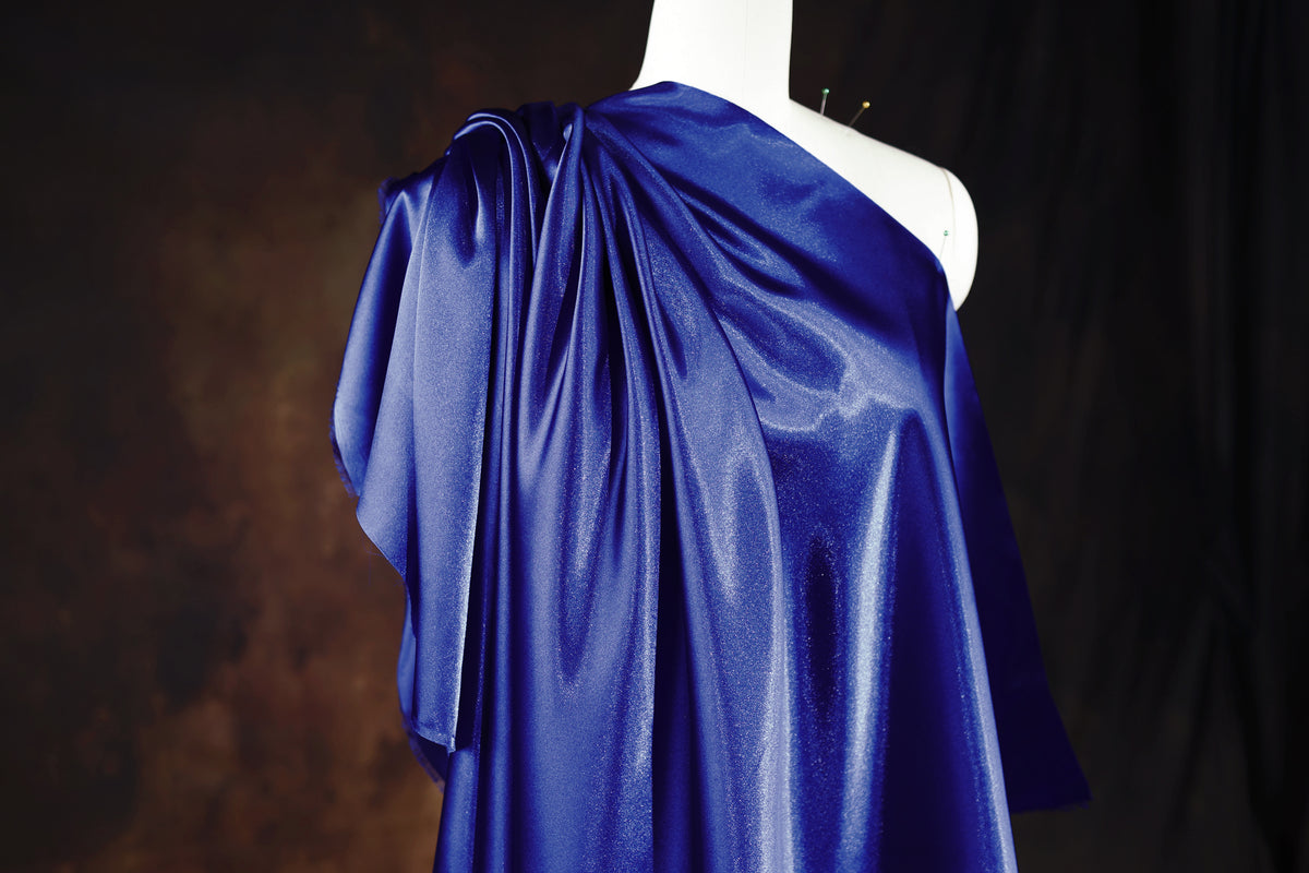 A mannequin wearing a blue one-shoulder dress with a draped, flowing fabric.