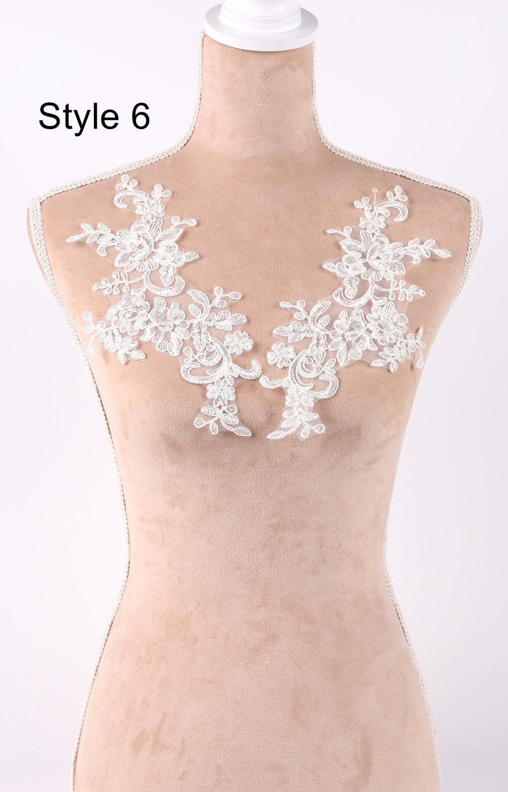A mannequin wearing a beige dress with white lace appliques on the shoulders.