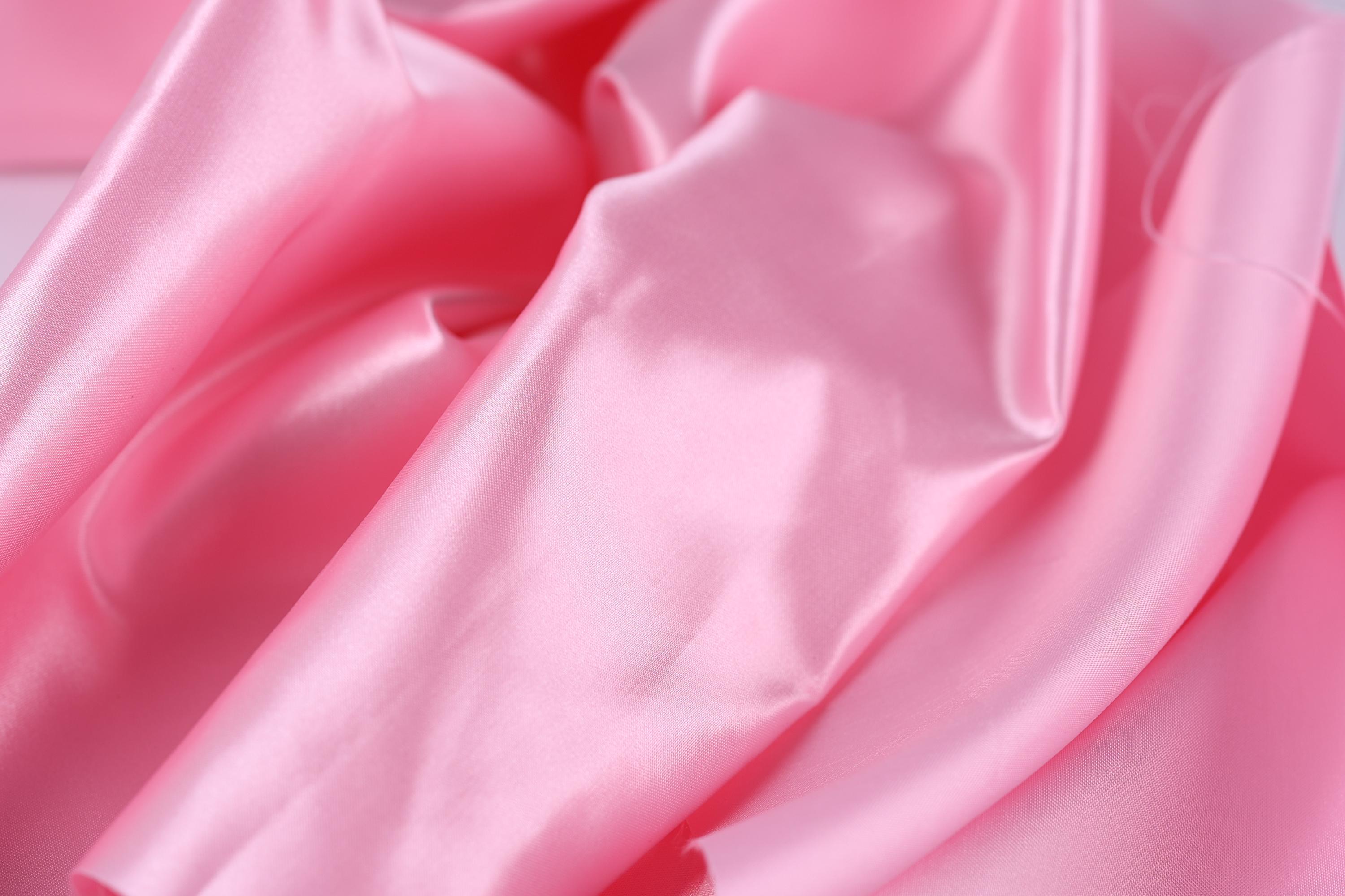 A close-up view of a soft, shiny pink satin fabric, with its folds and creases creating a textured and flowing appearance.
