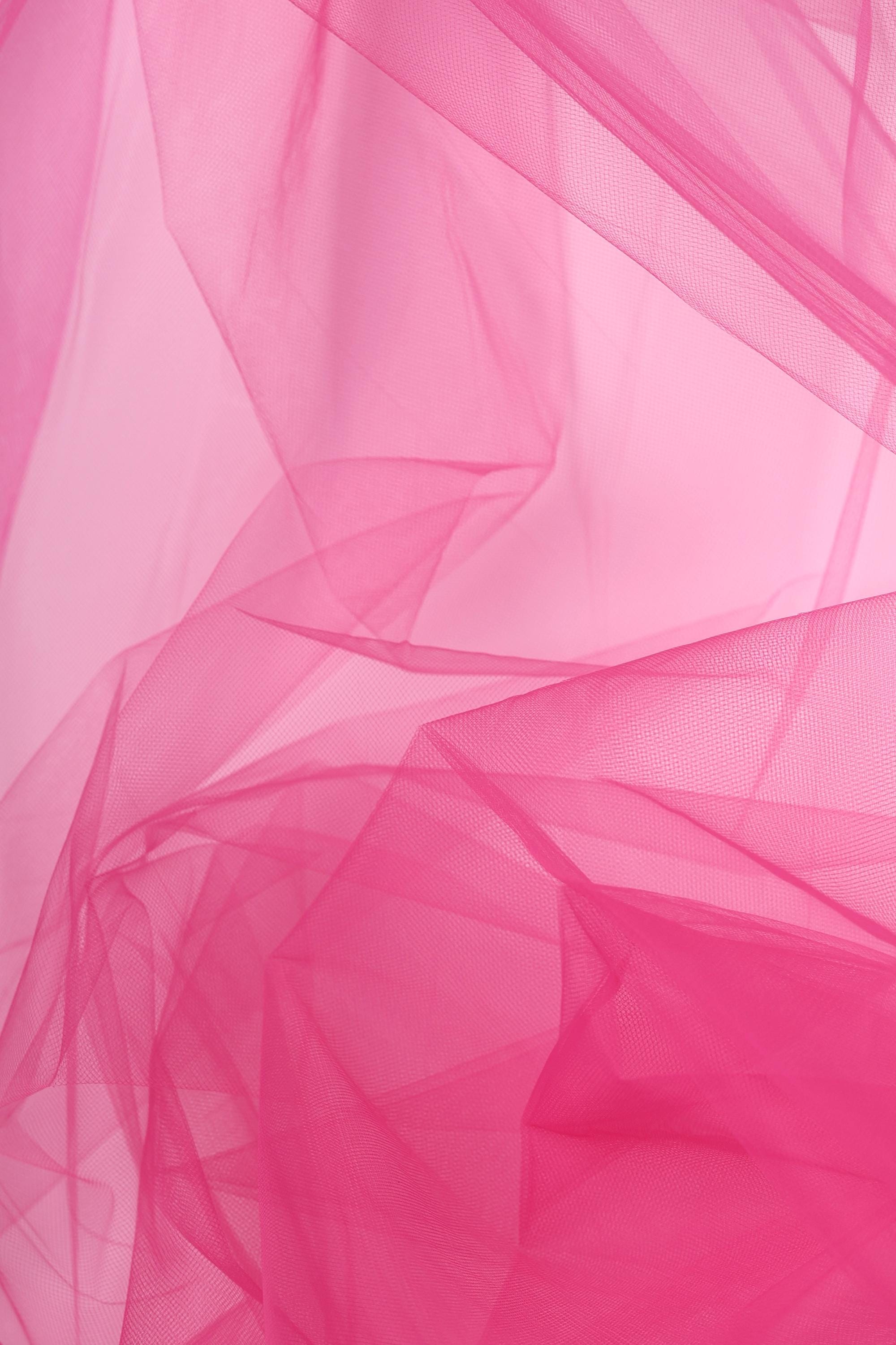 The image is a close-up of a pink fabric, possibly tulle, with a soft, flowing texture. The fabric appears to be slightly wrinkled, giving it a delicate and elegant appearance.