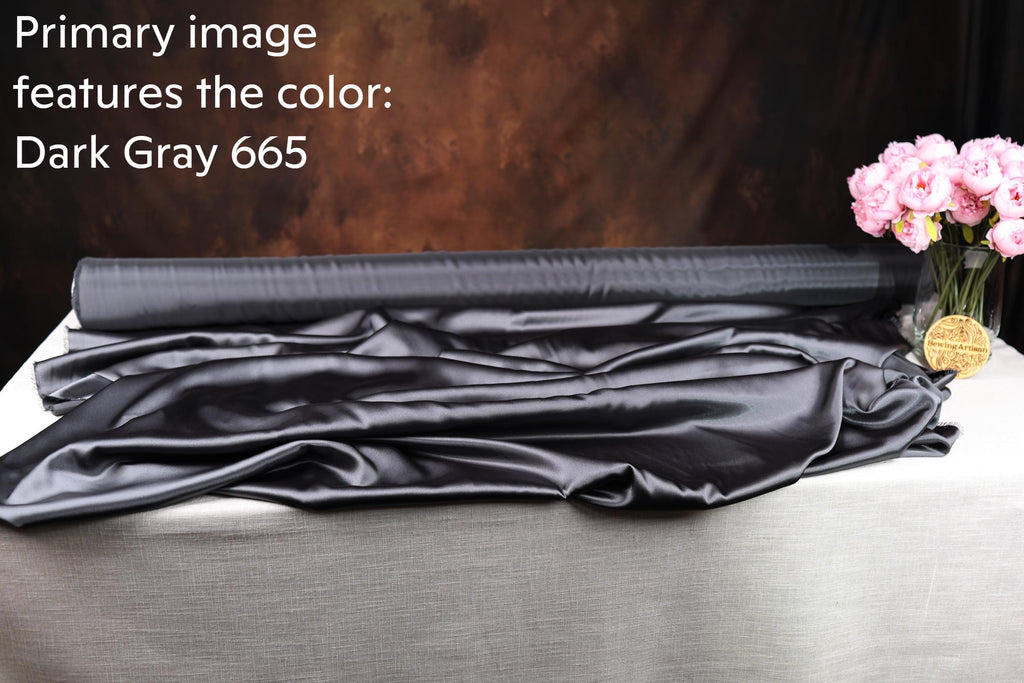 a roll of dark grey satin fabric with a vase of pink flowers on a table.