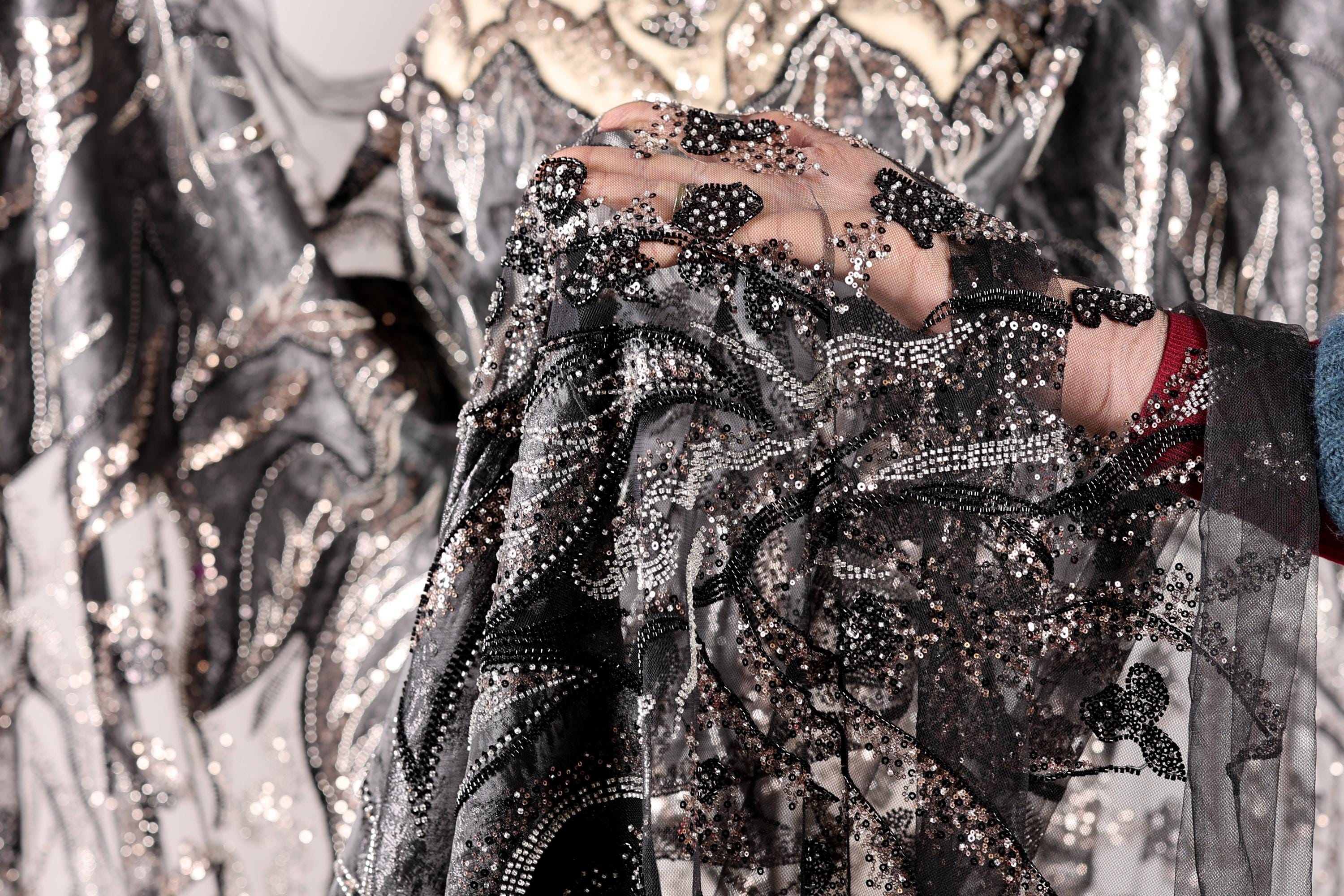 A close-up view of a hand holding a piece of black and silver fabric with intricate beading and embroidery.